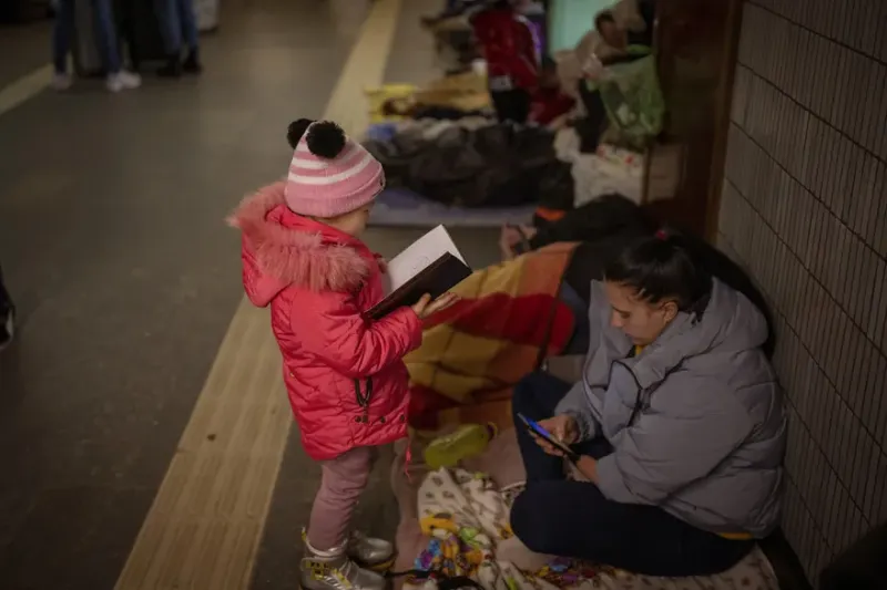 Una niña mira un cuaderno junto a su madre en el metro de Kiev, usándolo como refugio antiaéreo, en Ucrania.