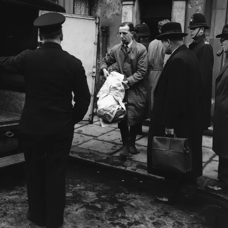 Un oficial de policía lleva varios huesos envueltos en periódicos hasta una furgoneta de policía que espera fuera del número 10 de Rillington Place, Londres. Los restos eran los de la quinta persona asesinada por el John Reginald Christie 