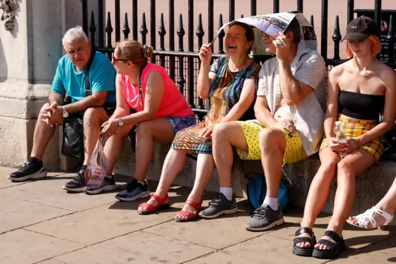 Las personas se refugian del sol debajo de un mapa durante el clima cálido, en las afueras del Palacio de Buckingham en Londres