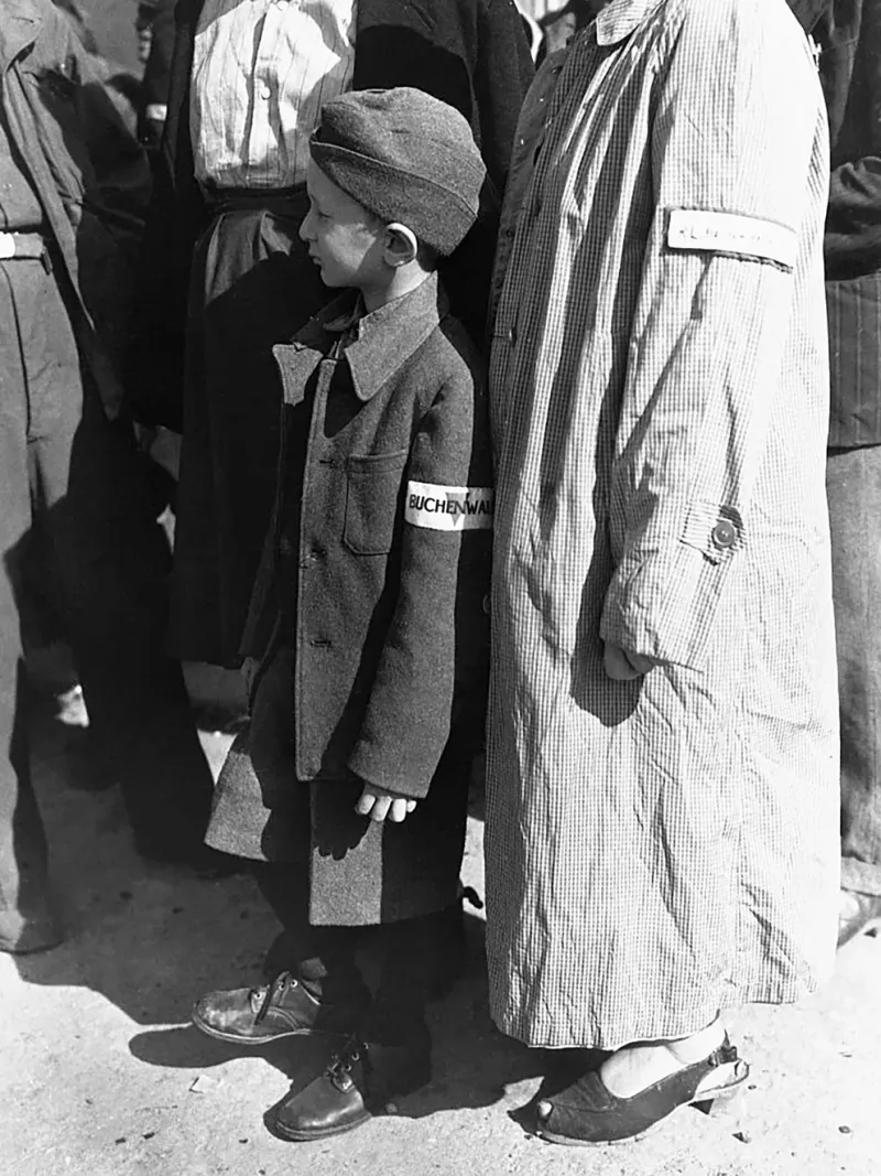  Un huérfano de guerra de seis años, con una insignia de Buchenwald en la manga, espera que lo llamen durante el pase de lista en el campamento de Buchenwald, Alemania, para partir hacia una nueva vida en Suiza al final de la Segunda Guerra Mundial