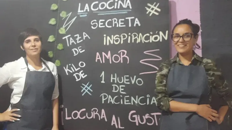  Adriana y Mariana frente al cartel que sienta las bases de cómo son los productos de Dulcemente