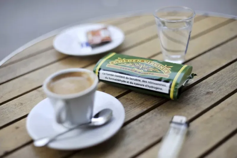 Una café, un paquete de tabaco, un mechero y vaso de agua sobre una mesa en un bar de París,